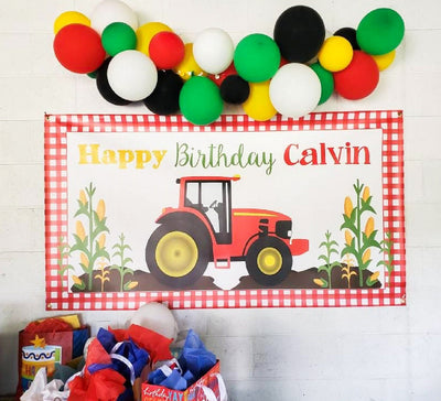 red tractor birthday banner with red gingham and corn stalks below a balloon garland