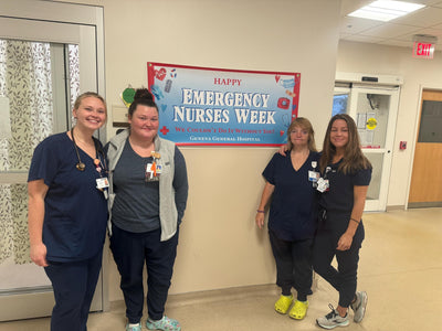 Happy Emergency Nurses Week banner at Geneva General Hospital. Four nurses in navy blue scrubs pose for a photo.  The banner features red, white, and blue colors and text.  The nurses are smiling and appear friendly.  The overall theme is appreciation for emergency nurses.