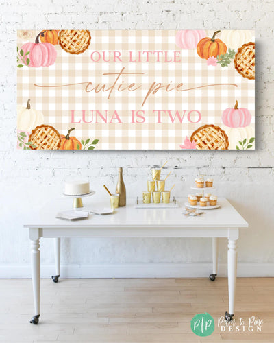 pink cutie pie birthday banner with fall pumpkins and lattice crust pies on gingham background in front of desser table
