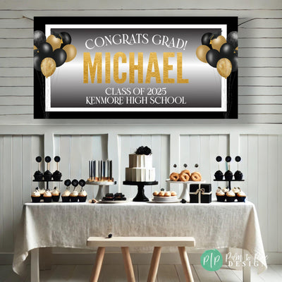 Custom graduation party banner in black, gold, and white featuring graduate’s name and school, celebratory grad cap balloons, and a clean modern border behind a simple black and white dessert table.
