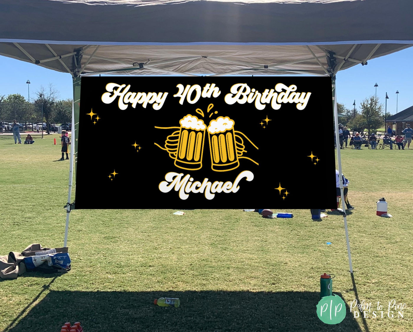 Black and gold Cheers and Beers birthday banner outdoors at party hanging under a pop up tent with white script Happy 40th Birthday name, and gold star accents.