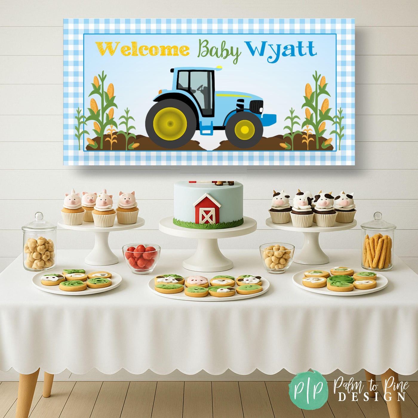 Personalized blue tractor baby shower banner with blue gingham border and wheat accents displayed as a backdrop behind a dessert table