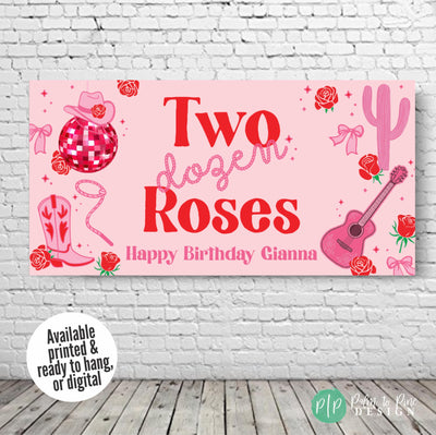 Pink and red Two Dozen Roses party banner featuring cowgirl and rope fonts, disco ball, roses, guitar, cactus, and cowgirl accessories, hung on a plain wall for birthday décor