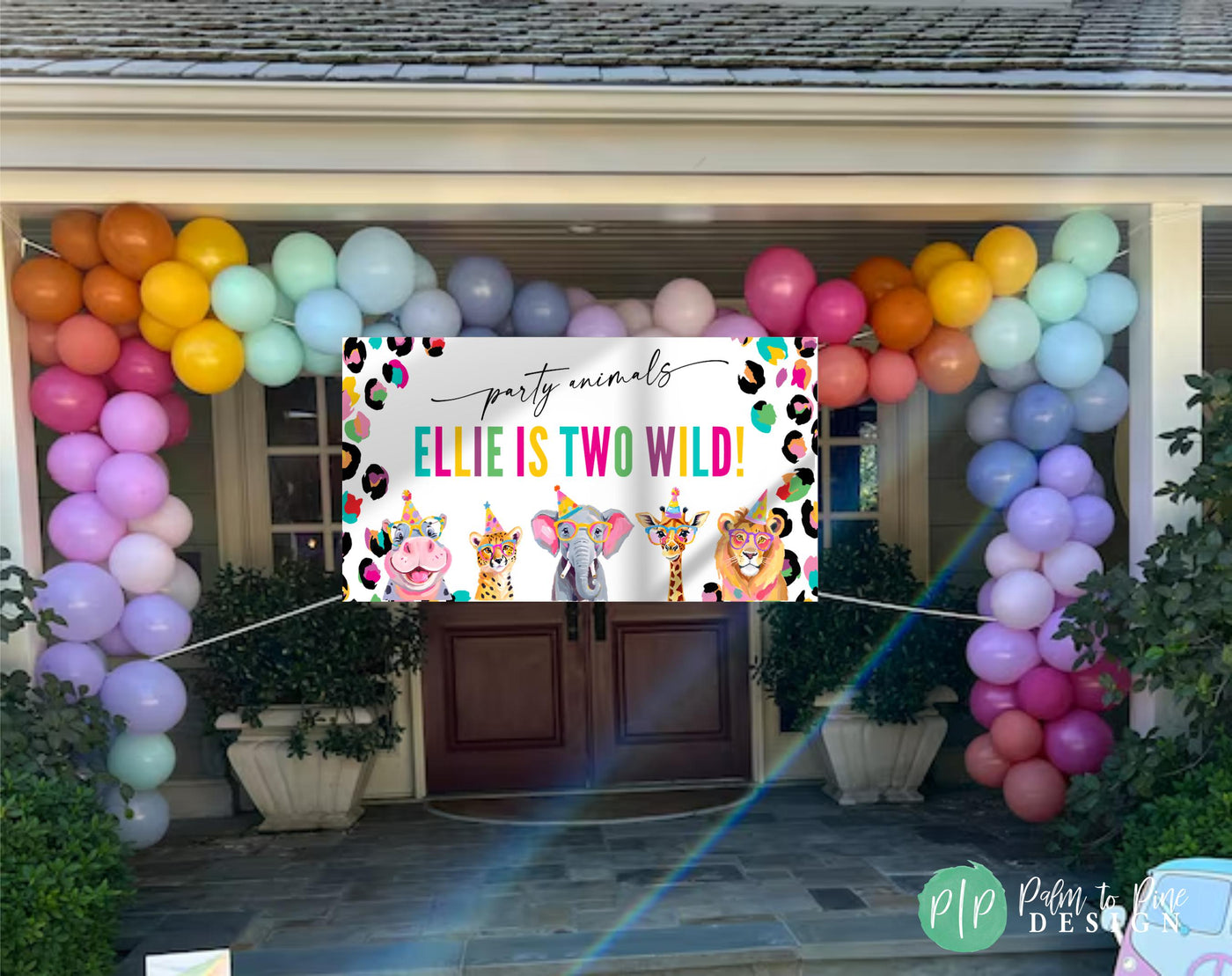 Bright rainbow cheetah print jungle banner with hippo, elephant, lion, cheetah, and giraffe in party hats hung outside house with colorful balloon garland