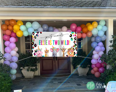 Bright rainbow cheetah print jungle banner with hippo, elephant, lion, cheetah, and giraffe in party hats hung outside house with colorful balloon garland